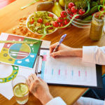 woman writing on chart with table of fresh produce nearby