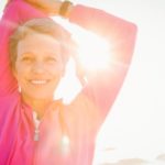 Happy woman stretches arms with sun coming through background