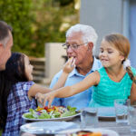 girl feeding grandfather at dinner outside