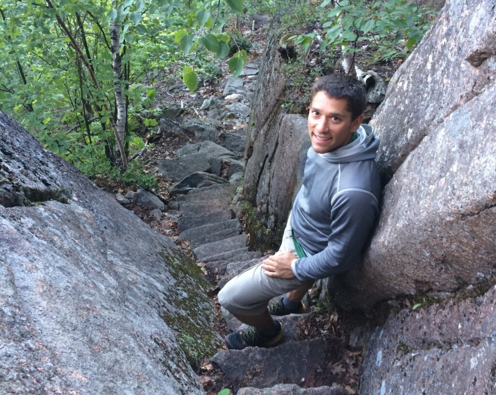 Mark Falender, a young man with dark hair and tan skin posing near large granite boulders - Backcountry Safety Summer Edition author image