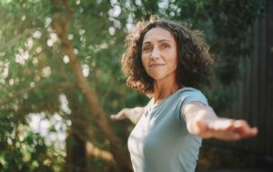 A woman in a green tee shirt doing yoga outdoors - embracing women's health featured image and middle age image