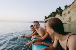 teen girls smiling as they balance on a surfboard together - embracing women's health teen image