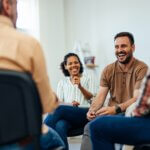 Focus on the smiling man, talking with people of all ages, during the group therapy. - the positive effects of sobriety on your health