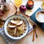 Autumn style breakfast with apple muesli bowl, coffee cup, book and candle, top view - healthy fall breakfast featured image