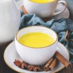 Golden turmeric milk with cinnamon sticks placed around mug