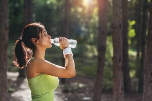 Girl drinking water from bottle in forest as part of taking care of your kidneys