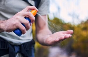Sunscreen spray, hand and closeup while hiking for security from the sun and health in summer. Exercise, nature and a man with a bottle with cream for skincare and safety from sunshine for fitness.
