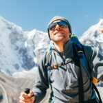 Portrait of smiling Hiker man on Taboche 6495m and Cholatse 6440m peaks background with trekking poles, UV protecting sunglasses. He enjoying mountain views during Everest Base Camp trekking route. proper eye care in the mountains